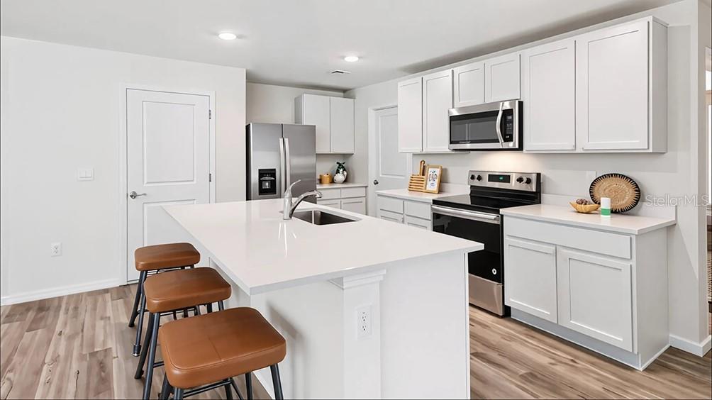 A modern kitchen features white cabinets, stainless steel appliances, a quartz island, and wood flooring — 9113 SW 47TH COURT, OCALA, FL