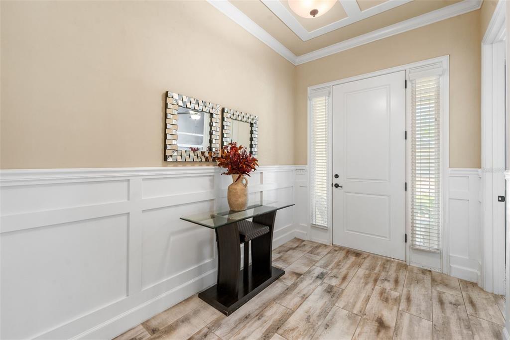 A foyer features white wainscoting, a glass console table, a mirror, and wood-look tile flooring — 13688 NW 12TH PLACE, NEWBERRY, FL