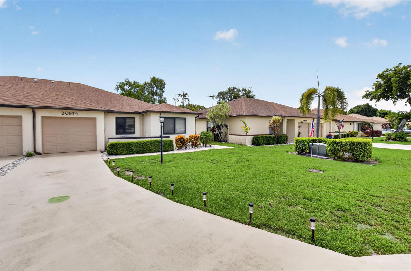 A view of the exterior of a single-story house with a concrete driveway and lawn — 20974 Concord Green Drive E, Boca Raton FL 33433, BOCA RATON, FL