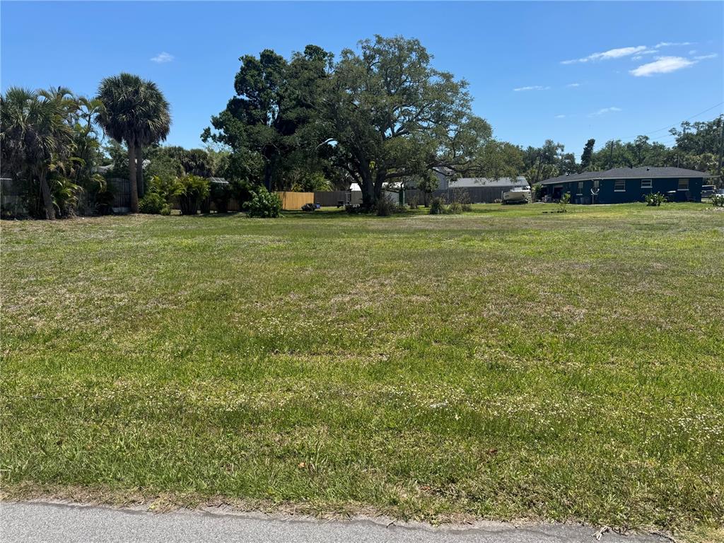 A grassy, vacant residential lot features several mature trees and a neighboring house — BONITO AVENUE, NOKOMIS, FL