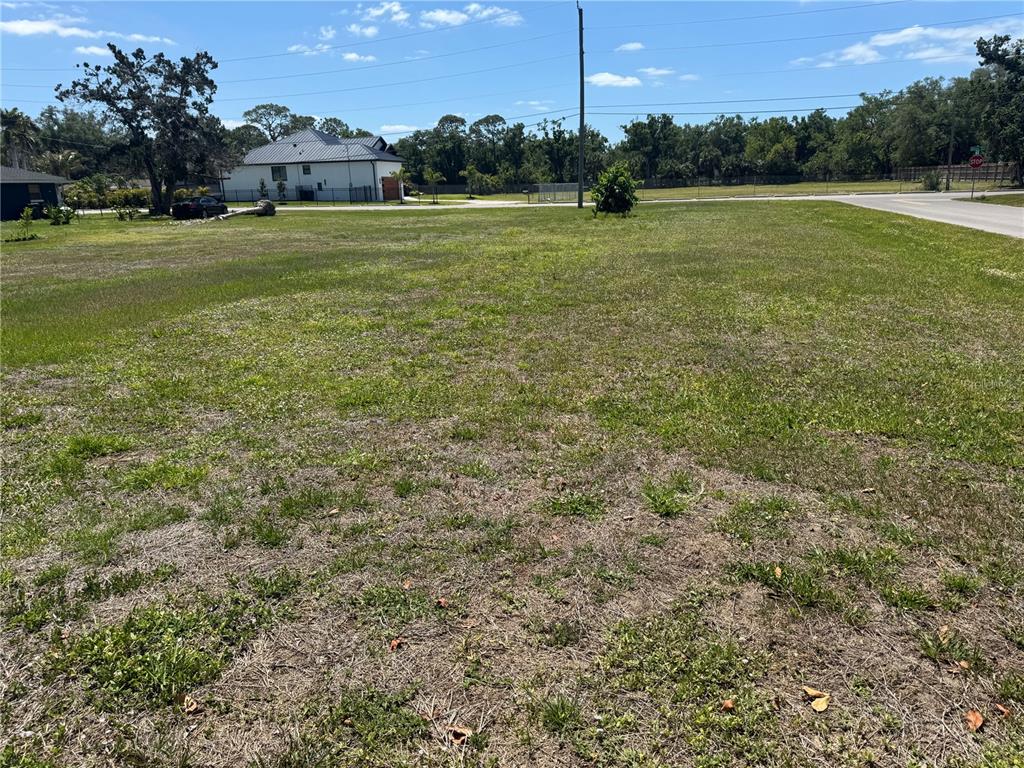 A vacant, grassy residential lot sits next to a paved road and a white house — BONITO AVENUE, NOKOMIS, FL