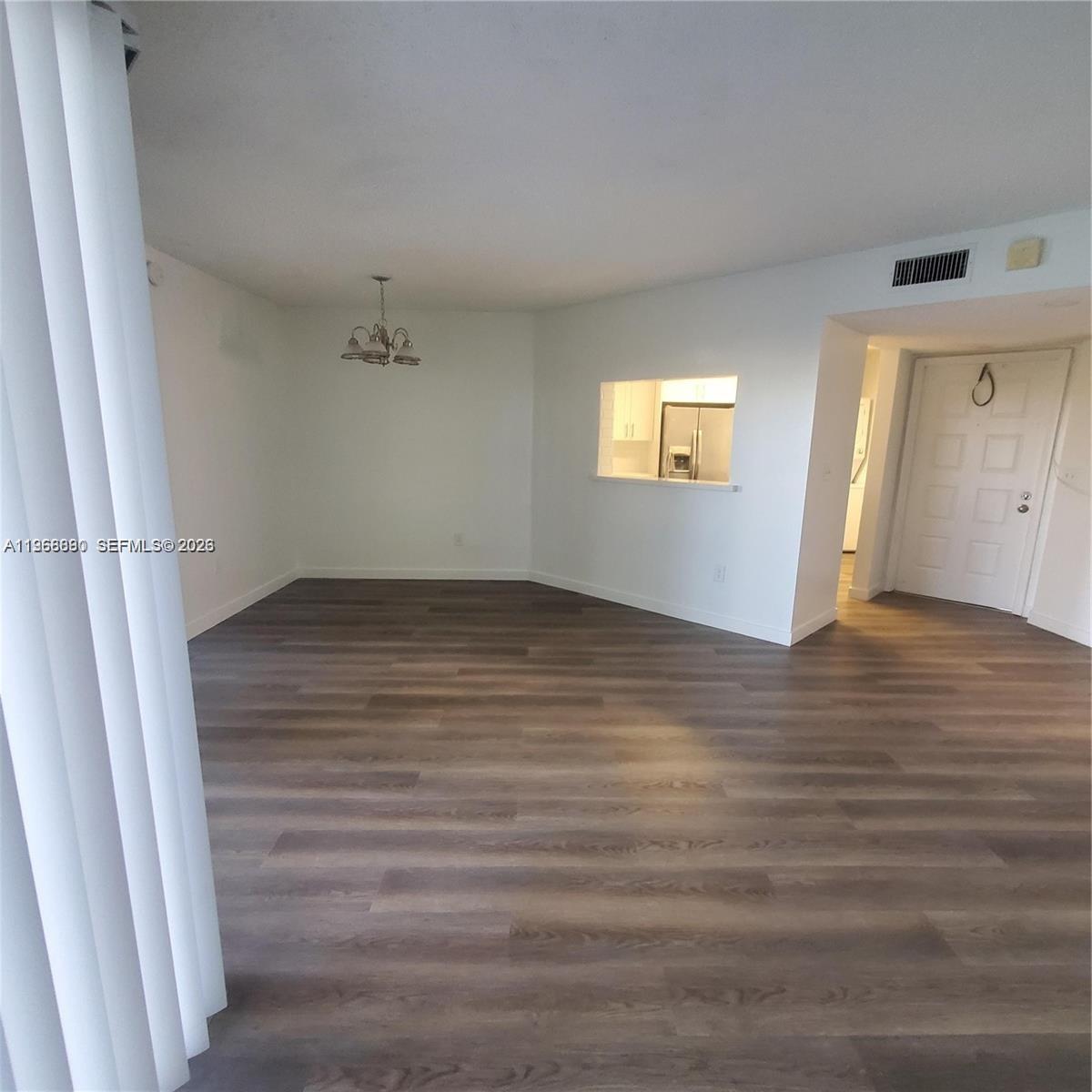 An empty living and dining area features wood-look flooring, white walls, and a kitchen pass-through — 929 Hamilton Dr # 929F, Homestead FL 33034, HOMESTEAD, FL