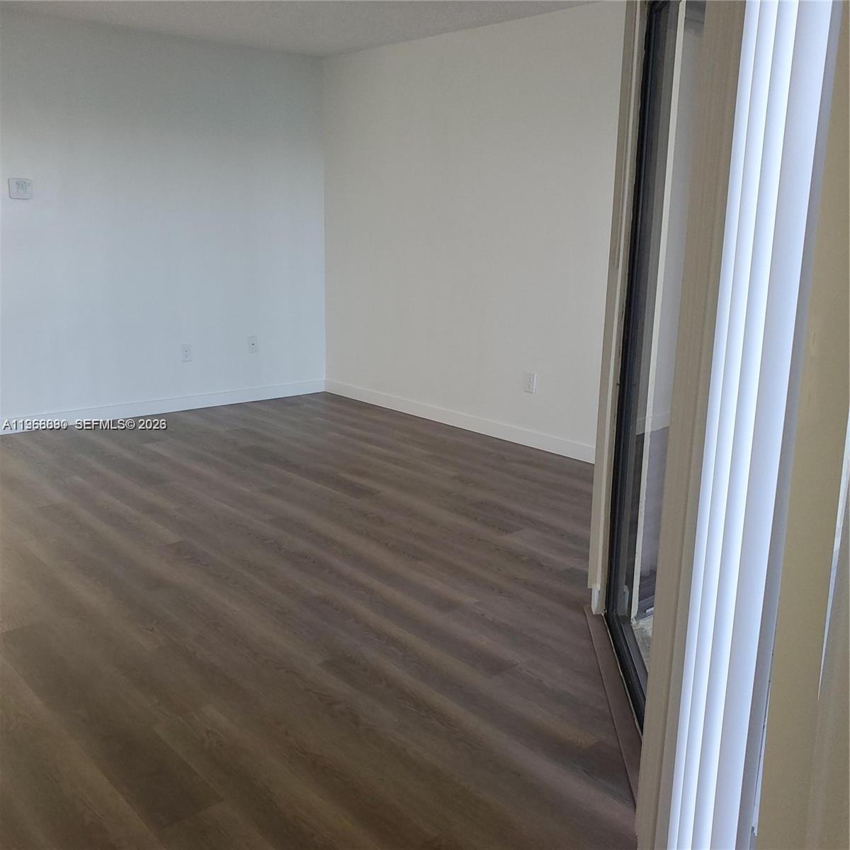 An empty room features white walls, dark wood-look flooring, and a sliding glass door — 929 Hamilton Dr # 929F, Homestead FL 33034, HOMESTEAD, FL