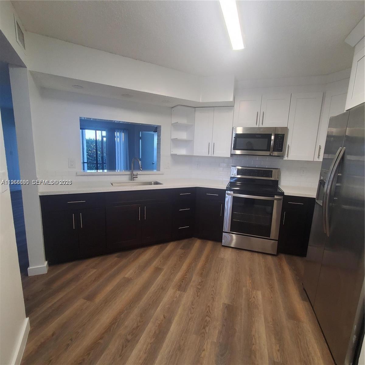 A kitchen features dark lower cabinets, white upper cabinets, stainless steel appliances, and wood-look flooring — 929 Hamilton Dr # 929F, Homestead FL 33034, HOMESTEAD, FL