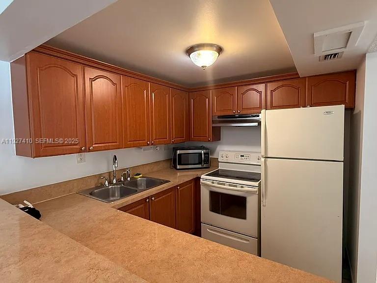 A kitchen features wood cabinets, a white refrigerator, a stove, and a tan countertop — 5855 Washington St # 91, Hollywood FL 33023, HOLLYWOOD, FL