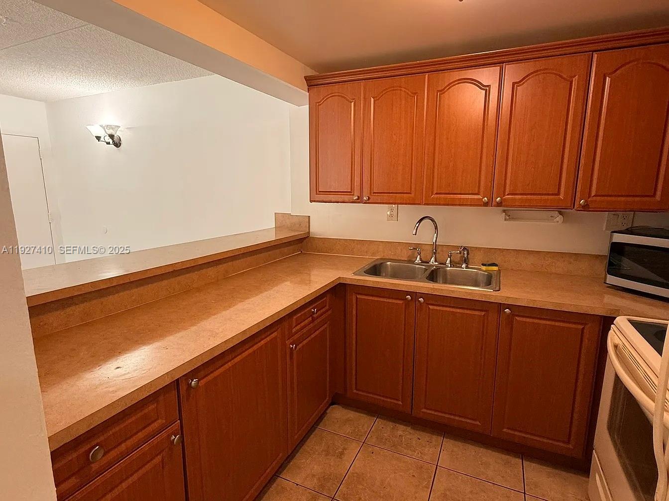 A kitchen features wood cabinets, a double-basin sink, and tan countertops over tile flooring — 5855 Washington St # 91, Hollywood FL 33023, HOLLYWOOD, FL