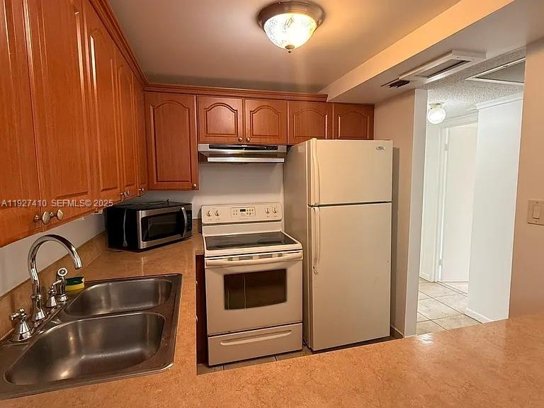 A kitchen features wood cabinets, a stainless steel sink, and white appliances — 5855 Washington St # 91, Hollywood FL 33023, HOLLYWOOD, FL