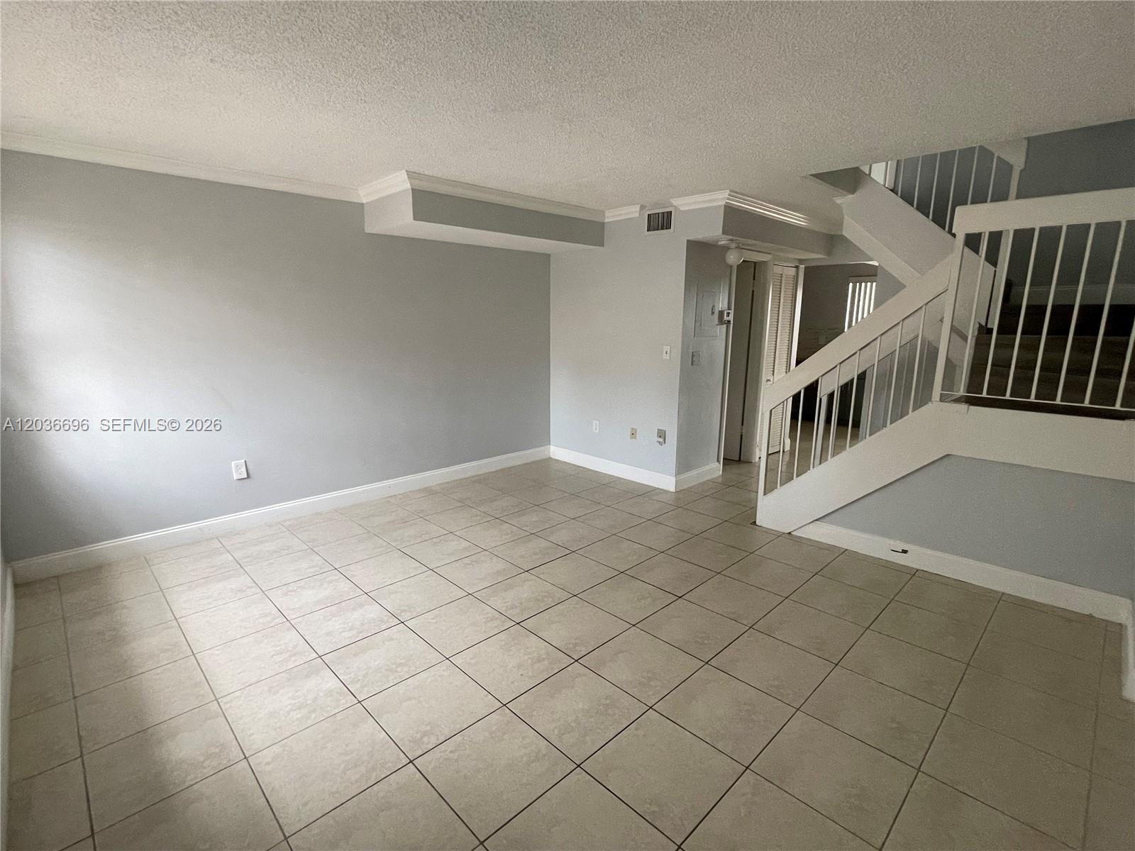 An empty living room features light-colored tile flooring, gray walls, and a white staircase — 7510 SW 152nd Ave # B202, Miami FL 33193, MIAMI, FL