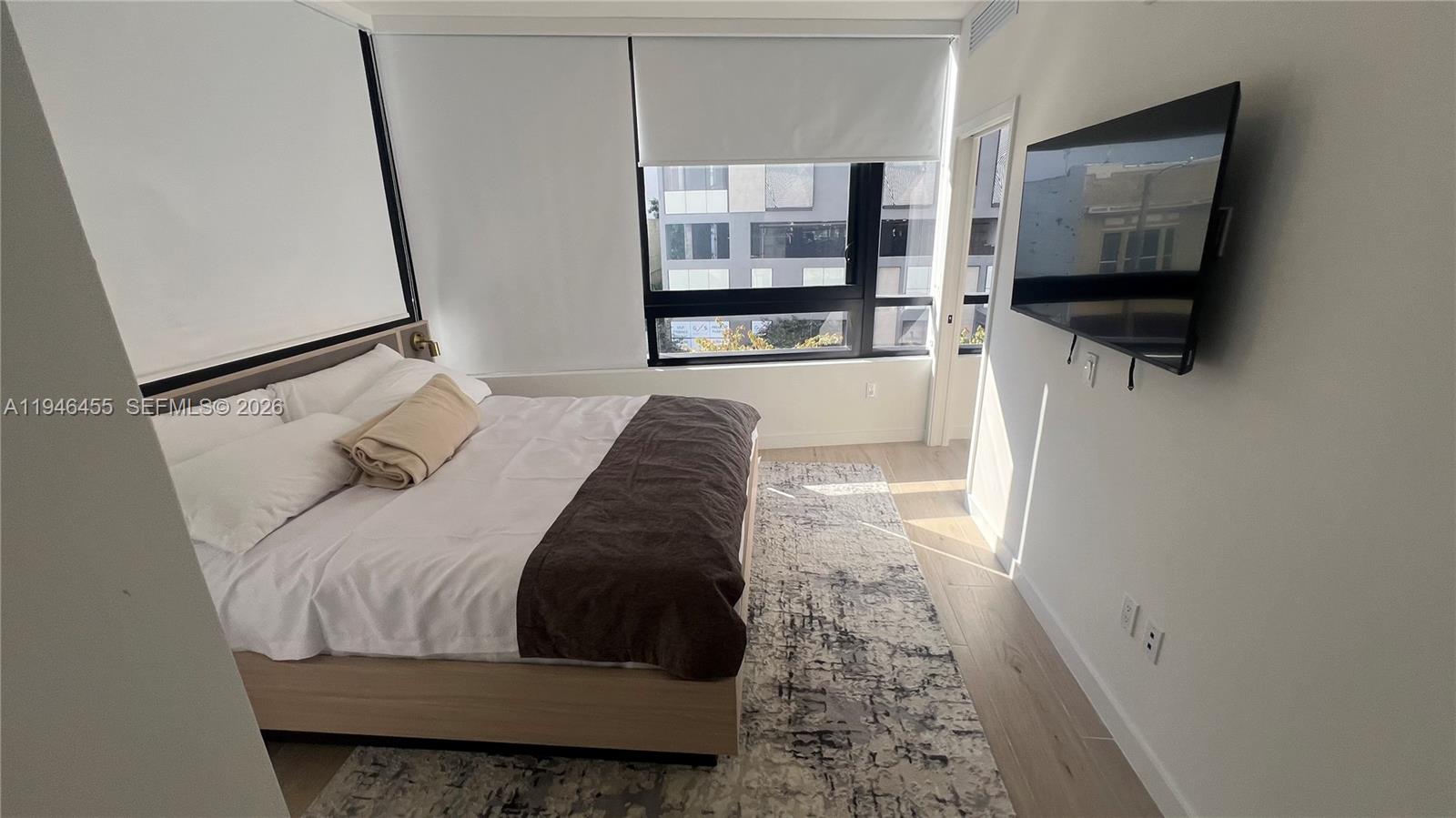 A bedroom features a bed with a dark runner, a wall-mounted television, and large windows — 225 N Miami Ave # 312, Miami FL 33128, MIAMI, FL