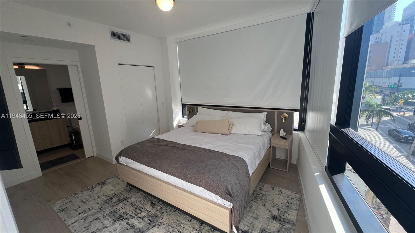 A bedroom features a bed, light wood flooring, a rug, and a city view window — 225 N Miami Ave # 312, Miami FL 33128, MIAMI, FL