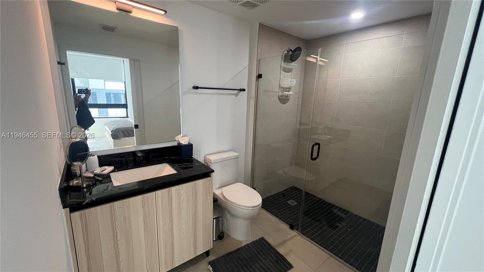 A modern bathroom features a black marble vanity, a glass-enclosed shower, and light wood cabinetry — 225 N Miami Ave # 312, Miami FL 33128, MIAMI, FL
