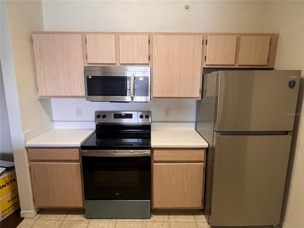 A kitchen features light wood cabinets, white countertops, and stainless steel appliances — 5459 VINELAND RD UNIT 4310, ORLANDO, FL