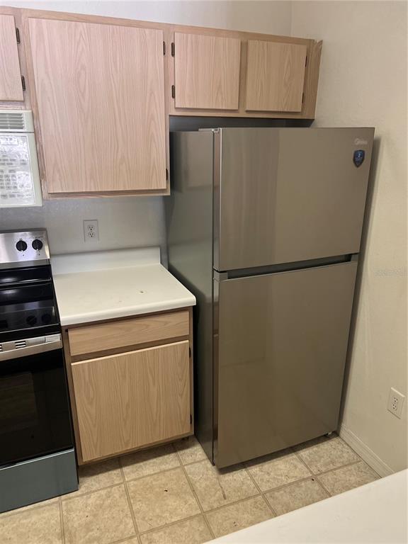 A kitchen features light wood cabinets, a stainless steel refrigerator, and a white countertop — 5459 VINELAND RD UNIT 4310, ORLANDO, FL