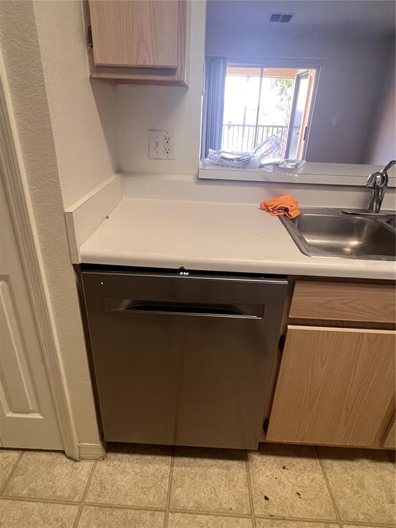 A kitchen features a stainless steel dishwasher, light-colored countertops, and wood-toned cabinets — 5459 VINELAND RD UNIT 4310, ORLANDO, FL