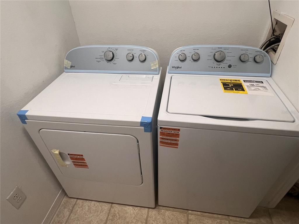 A white Whirlpool clothes dryer and washing machine sit side-by-side in a laundry room — 5459 VINELAND RD UNIT 4310, ORLANDO, FL
