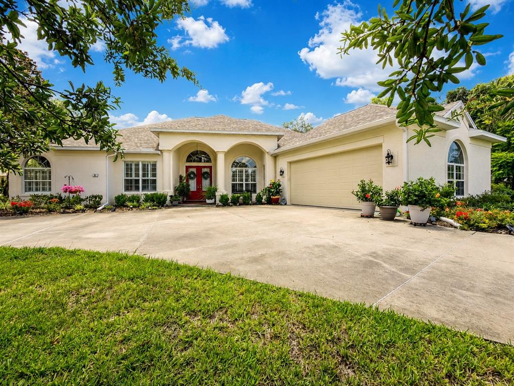 A single-story house with a beige stucco exterior, a red front door, and a concrete driveway — 8 COSMOS COURT E, HOMOSASSA, FL