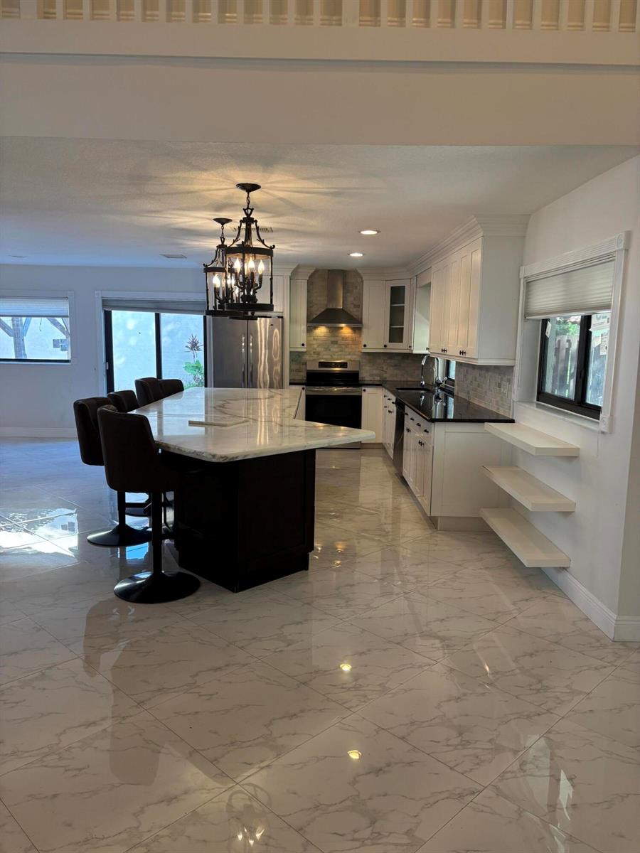 A modern kitchen features a dark island with marble countertops, white cabinetry, and tiled flooring — 2199 Charleston, Weston FL 33326, WESTON, FL