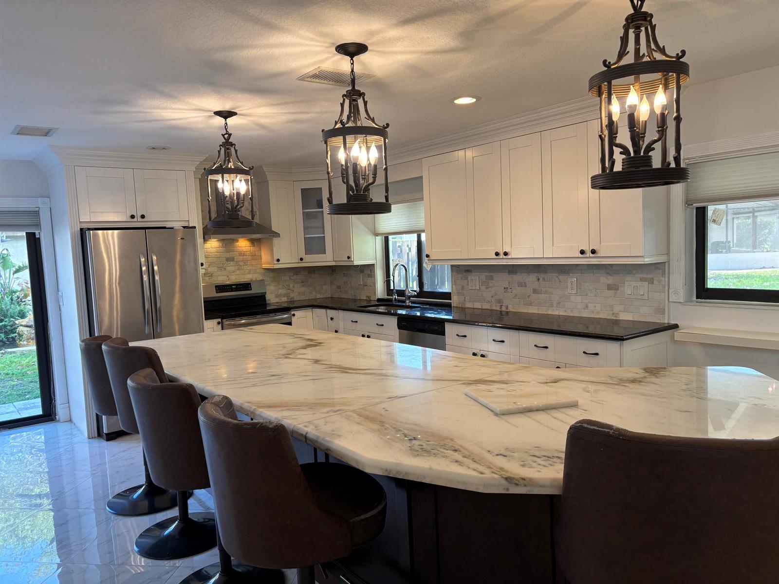 A kitchen features white cabinetry, a large marble-topped island, and three hanging lantern-style lights — 2199 Charleston, Weston FL 33326, WESTON, FL