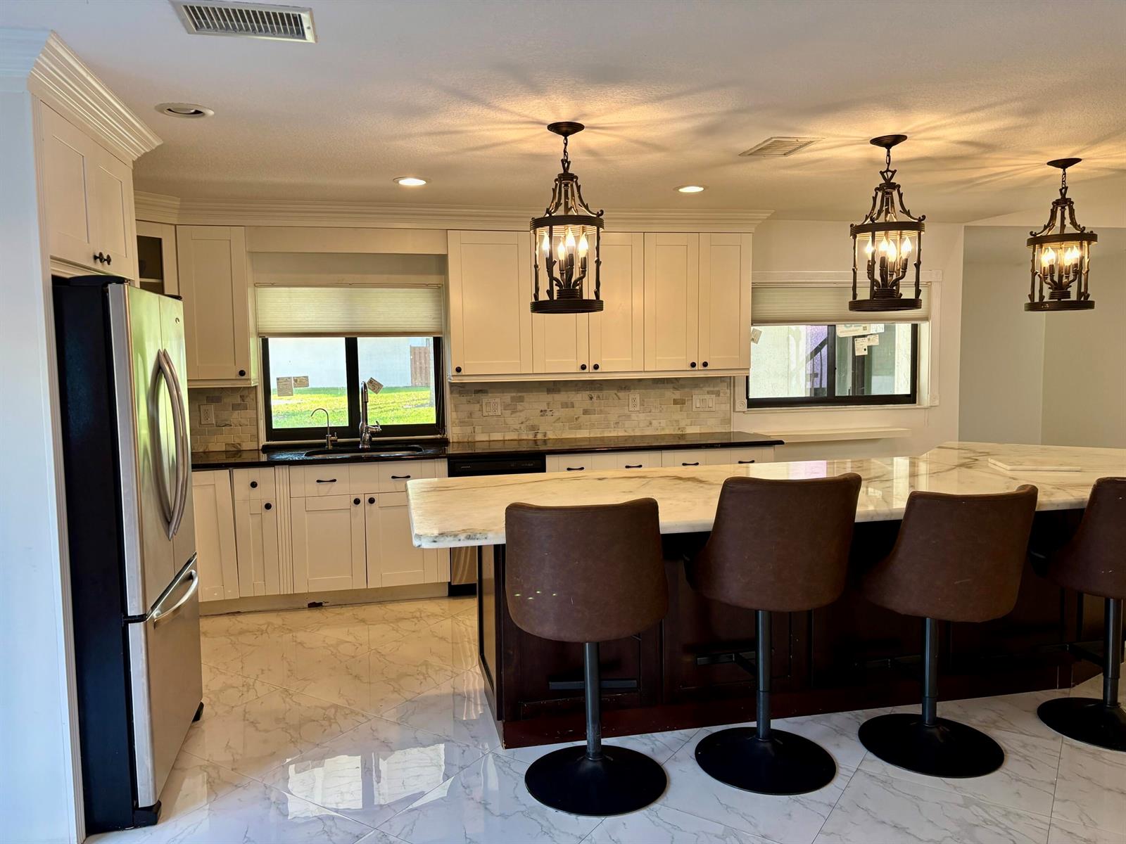 A kitchen features white cabinets, a dark island with bar stools, and marble-style tile flooring — 2199 Charleston, Weston FL 33326, WESTON, FL