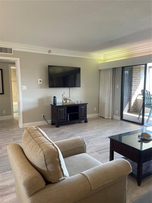 A living room features light wood-look flooring, a wall-mounted television, and a sliding glass door — 36750 US HIGHWAY 19 N UNIT 14-211, PALM HARBOR, FL
