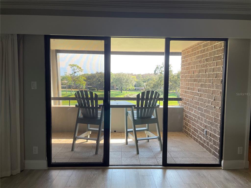A sliding glass door opens to a balcony with two chairs overlooking a grassy area — 36750 US HIGHWAY 19 N UNIT 14-211, PALM HARBOR, FL