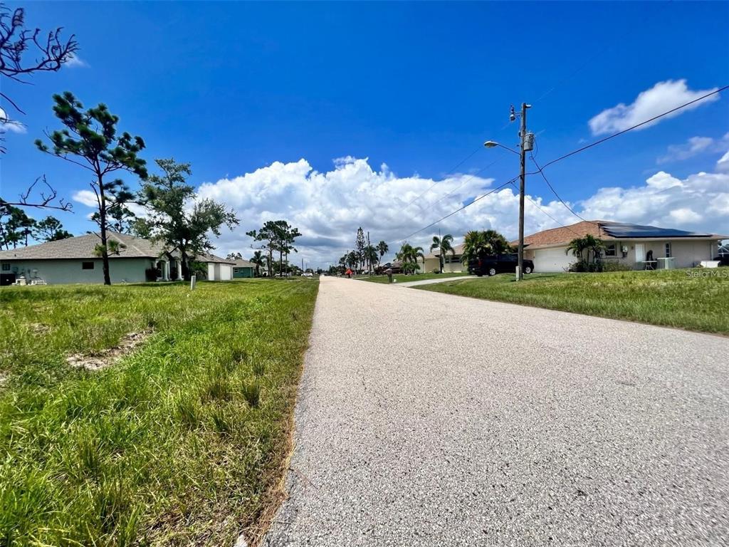 A paved residential street lined with houses, green lawns, and utility poles under a blue sky — 230 FAIRWAY ROAD, ROTONDA WEST, FL