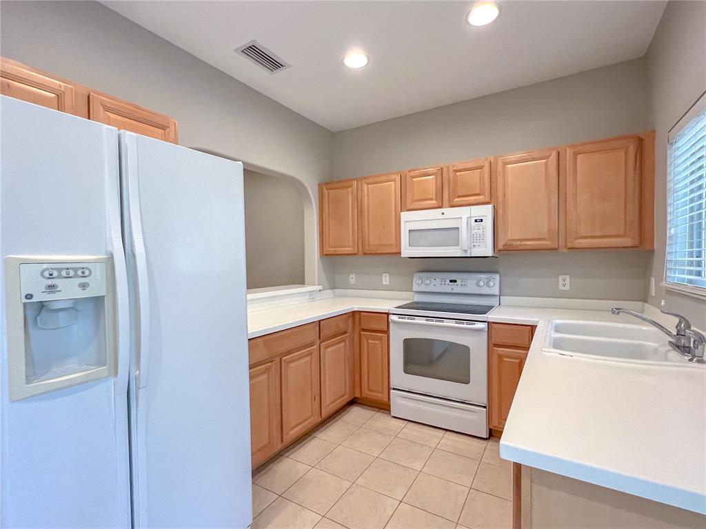 A kitchen features light wood cabinets, white appliances, white countertops, and beige tile flooring — 267 CAPE HARBOUR LOOP UNIT 103, BRADENTON, FL