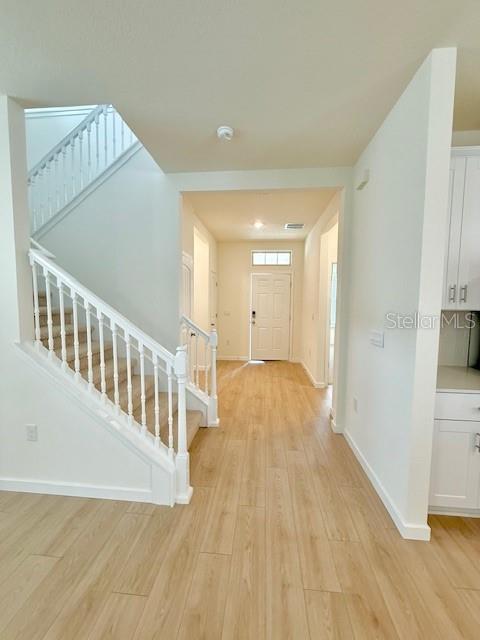 A bright entryway features light wood-look flooring, a white staircase, and a view toward the front door — 16827 HOBE SOUND COURT, WINTER GARDEN, FL