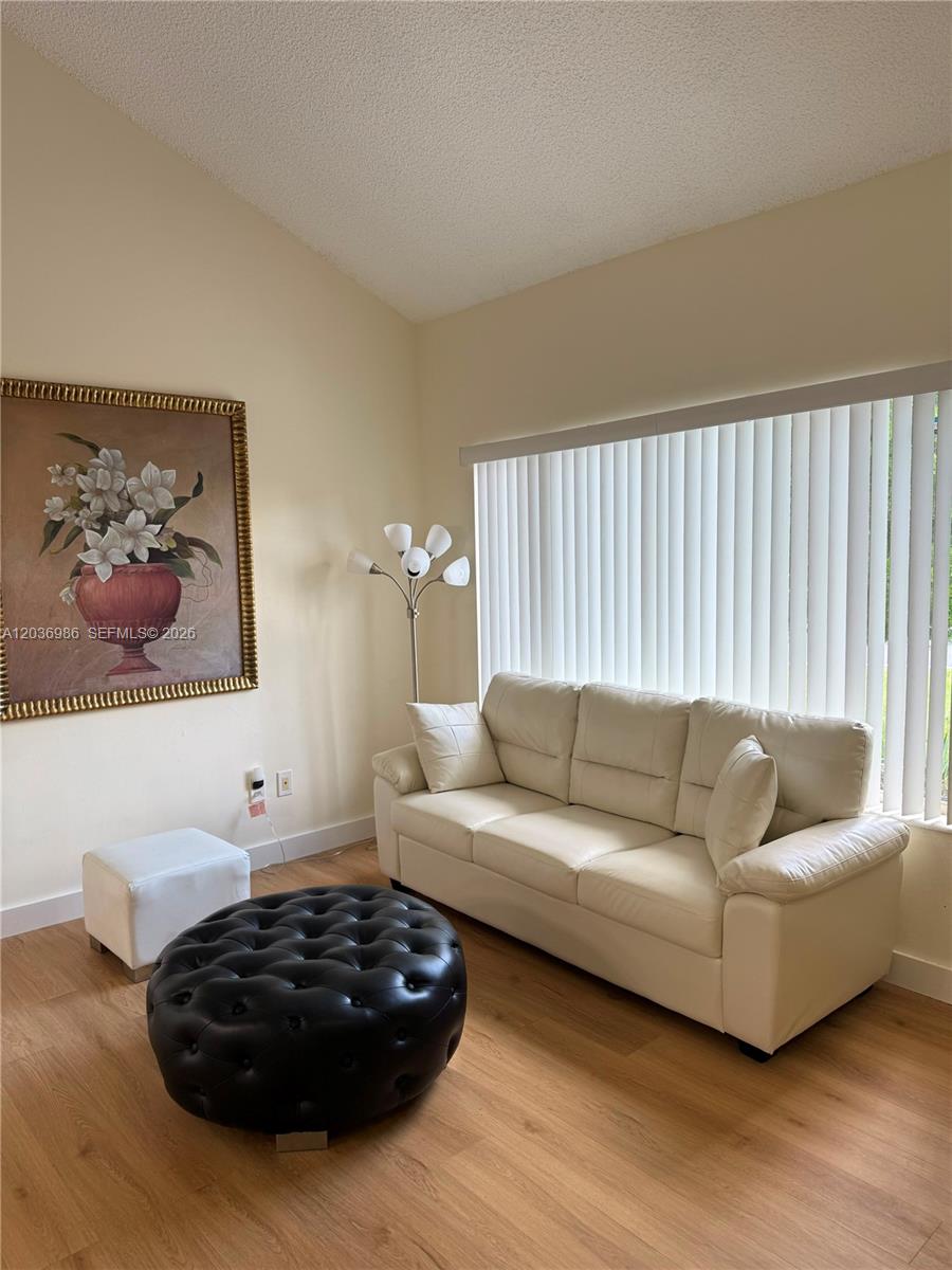 A living room features light wood flooring, a white sofa, a black ottoman, and wall art — 14795 SW 97th Ter # 0, Miami FL 33196, MIAMI, FL