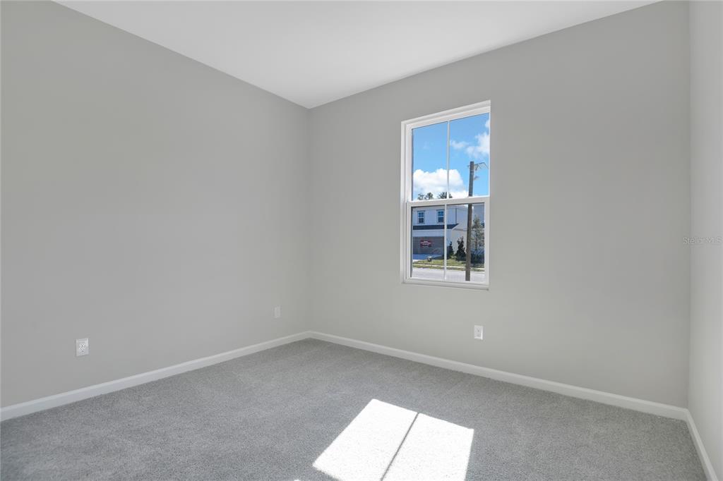 An empty bedroom features light gray walls, gray carpeting, and a single window — 1737 CARNELIAN STREET, DELAND, FL
