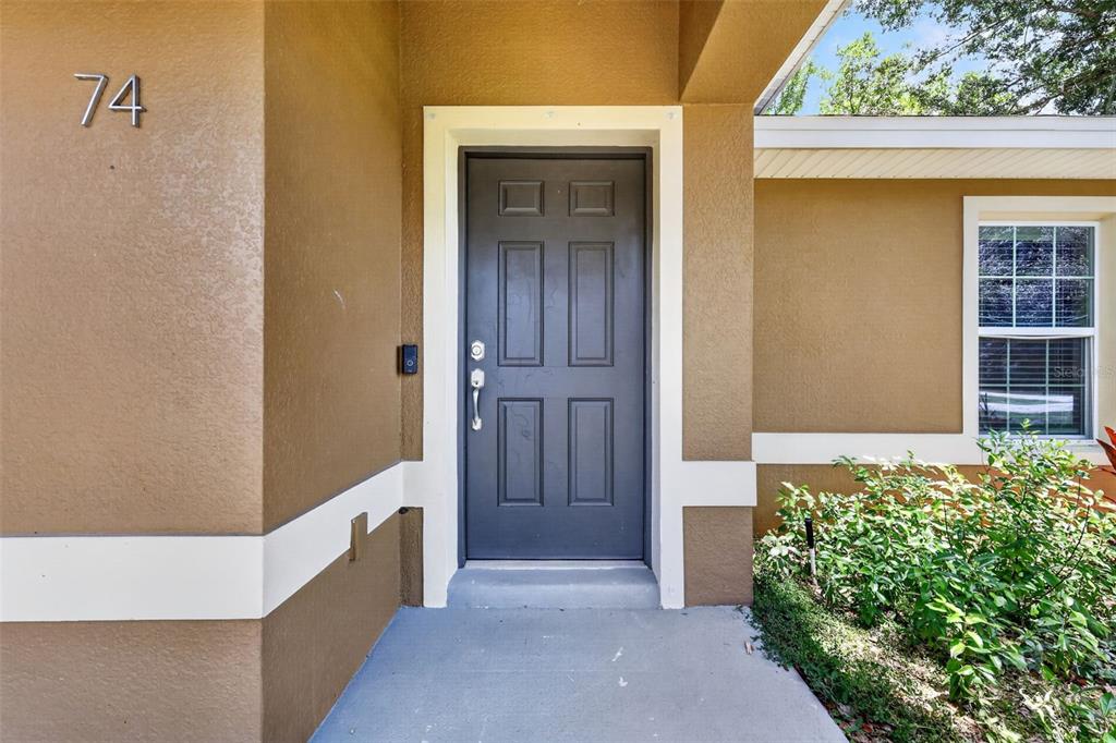 A dark gray front door with a white frame sits on a covered concrete porch — 74 N OAK AVENUE, UMATILLA, FL
