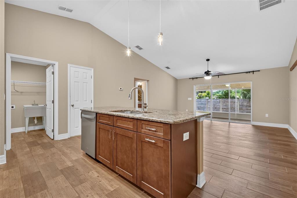 A kitchen island with granite countertops sits in an open-concept room with wood-look tile flooring — 74 N OAK AVENUE, UMATILLA, FL