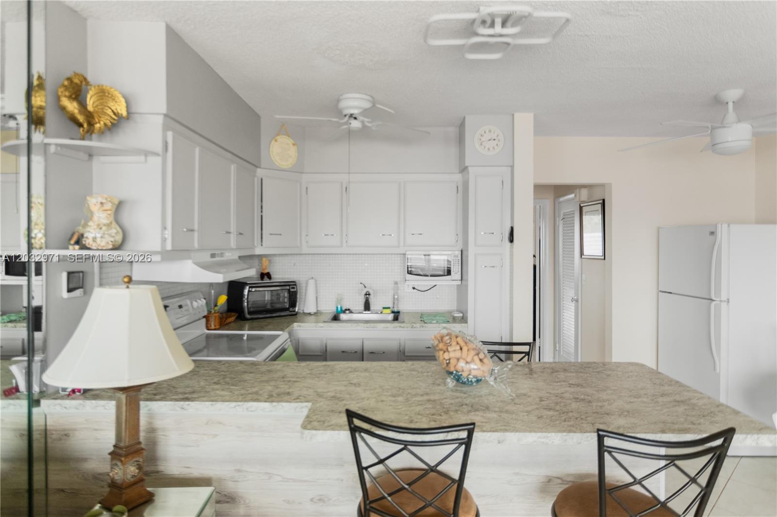A kitchen features light gray cabinets, a breakfast bar with stools, and white appliances — 725 SW 11th Ave # 12, Hallandale Beach FL 33009, HALLANDALE BEACH, FL