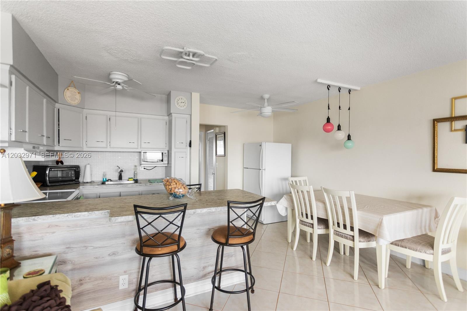 A kitchen with white cabinets and a breakfast bar opens into a dining area — 725 SW 11th Ave # 12, Hallandale Beach FL 33009, HALLANDALE BEACH, FL