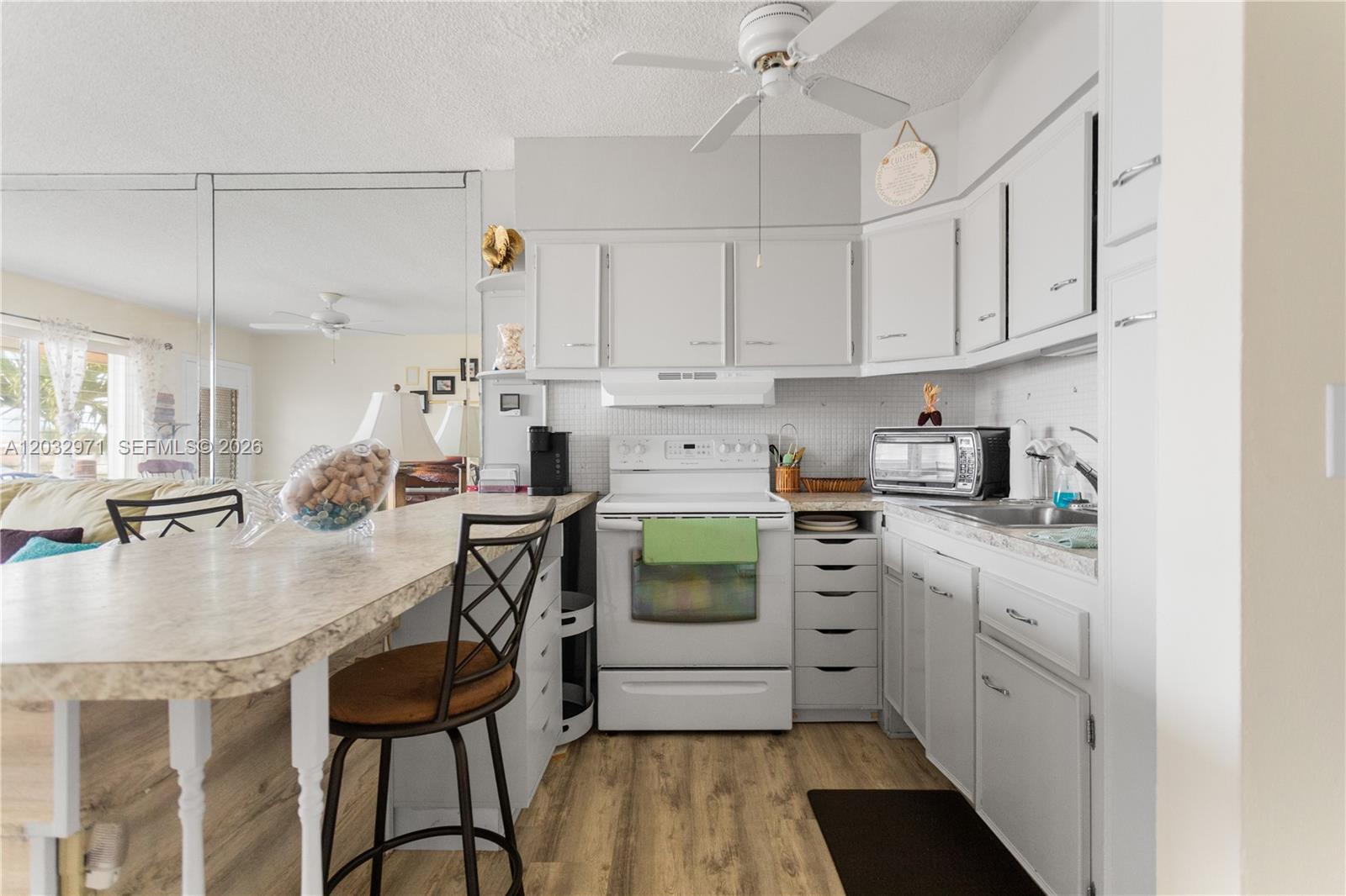 A kitchen features white cabinets, a white stove, a breakfast bar, and wood-look flooring — 725 SW 11th Ave # 12, Hallandale Beach FL 33009, HALLANDALE BEACH, FL