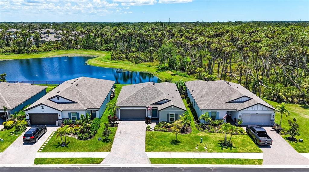 An aerial view shows three suburban houses with driveways situated near a pond and trees — 5413 BADINI WAY, PALMETTO, FL