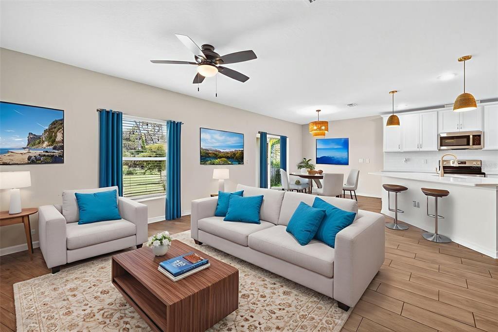 An open-concept living room and kitchen featuring light wood floors, white cabinetry, and blue accents — 5413 BADINI WAY, PALMETTO, FL