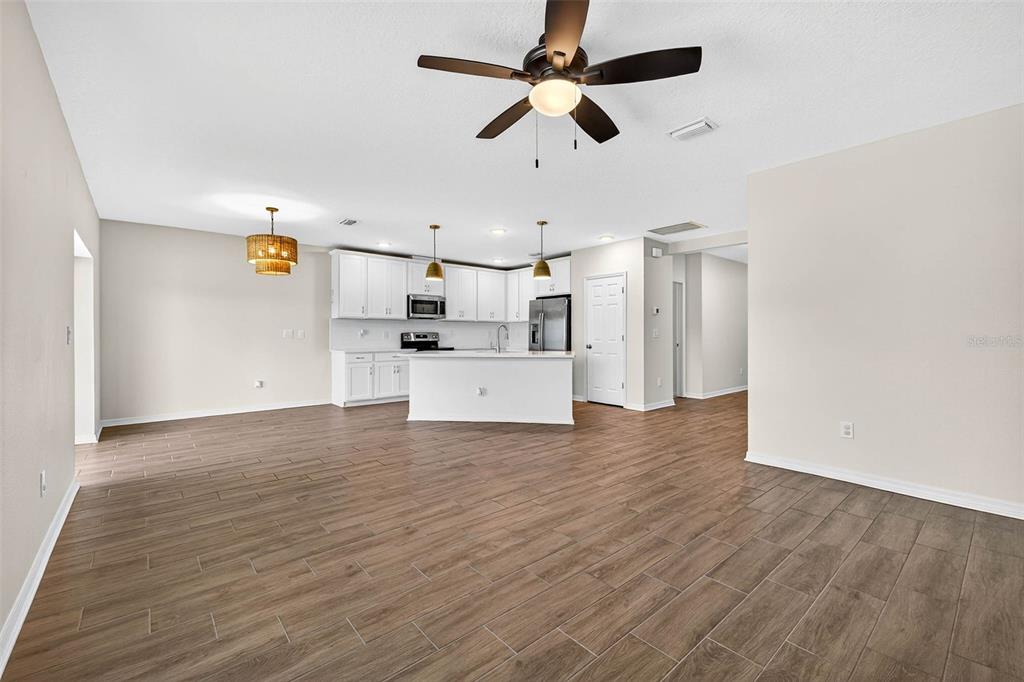An open-concept kitchen and living area features white cabinetry, a center island, and wood-look flooring — 5413 BADINI WAY, PALMETTO, FL
