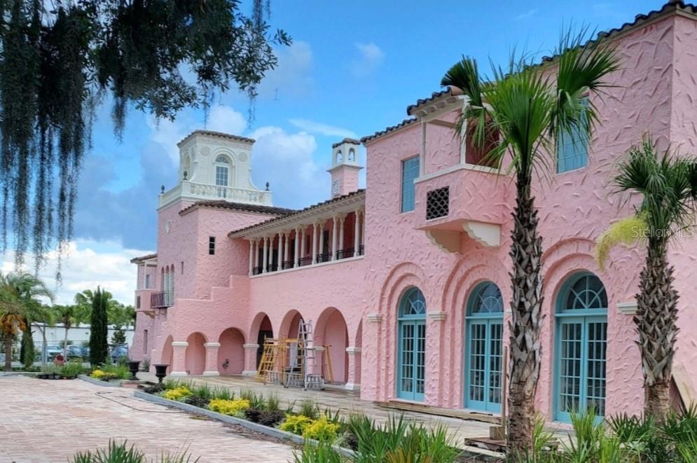 A pink Mediterranean-style mansion features arched doorways, a tower, and a balcony under a blue sky — 6313 OELSNER STREET, NEW PORT RICHEY, FL