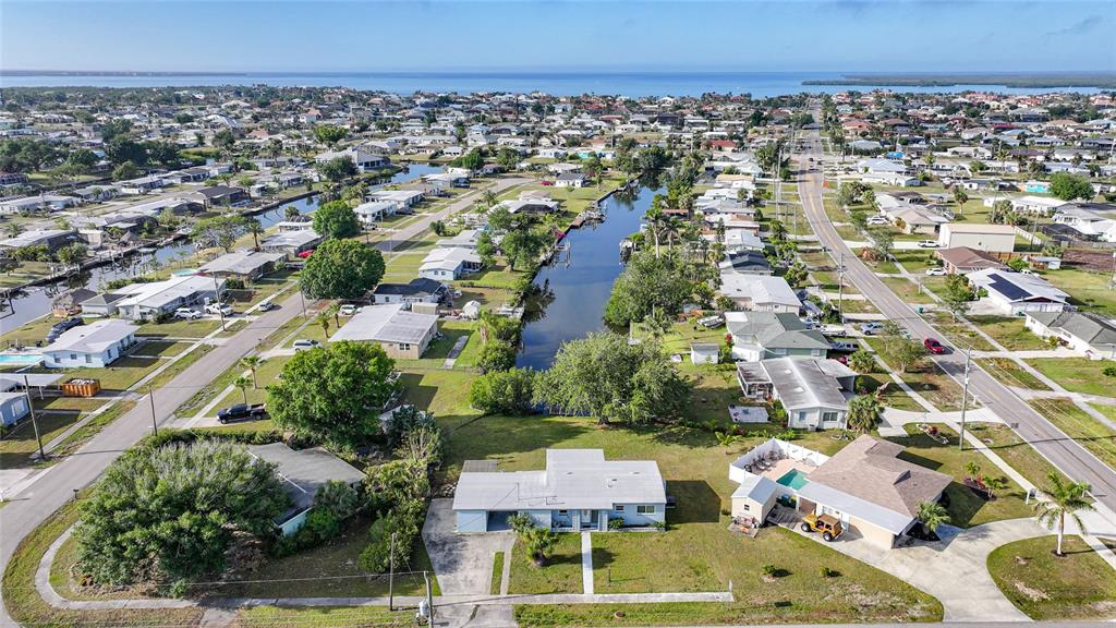 An aerial view shows a residential neighborhood with houses, a central canal, and distant water — 21249 HIGGS DRIVE, PORT CHARLOTTE, FL