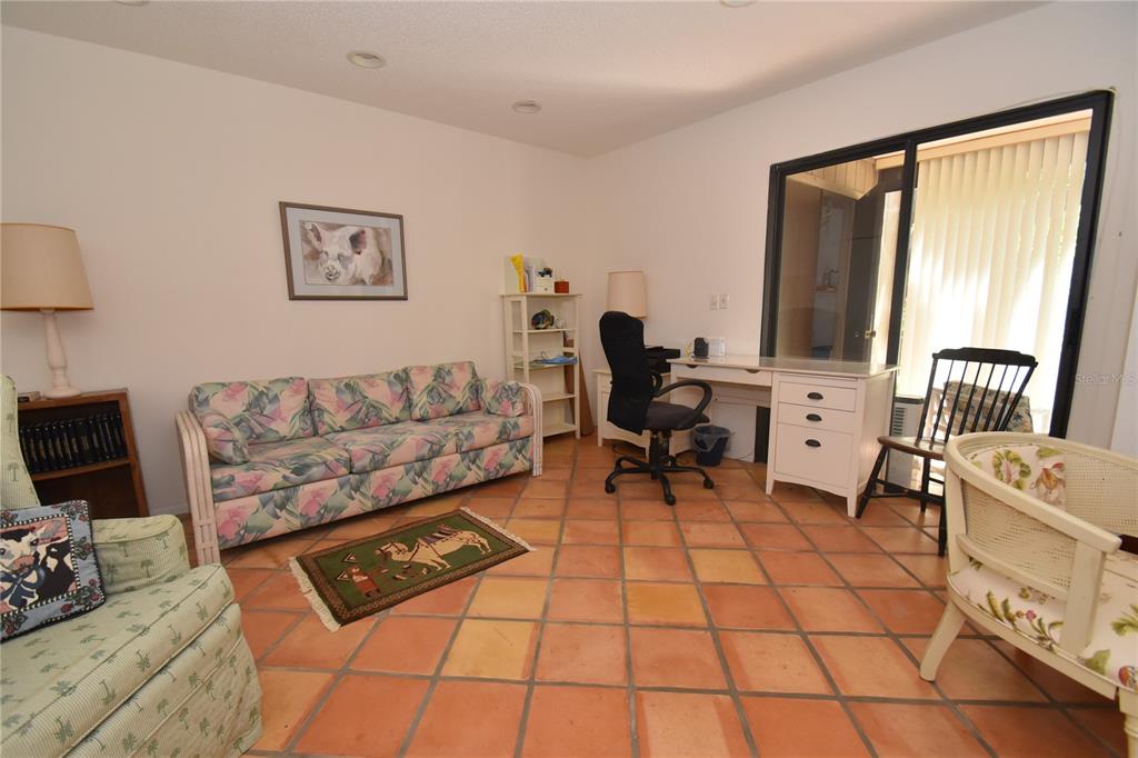 A room with a floral sofa, desk, chair, and terracotta tile flooring — 1626 BROOKHOUSE DRIVE UNIT BR137, SARASOTA, FL