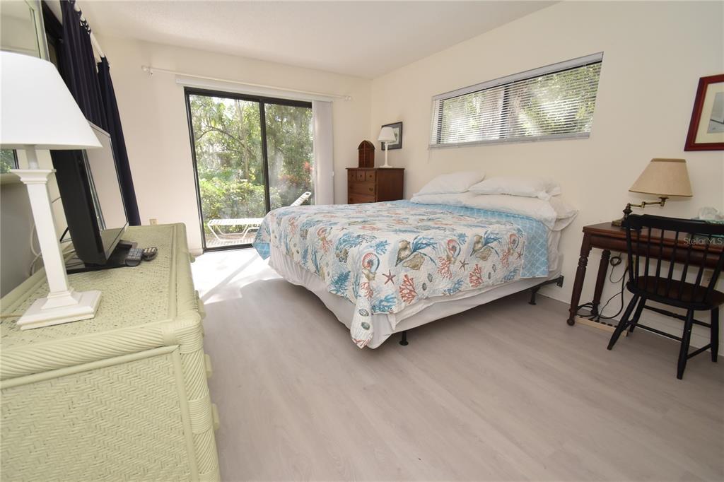 A bedroom with light wood-look flooring, a queen bed, a desk, and a sliding glass door — 1626 BROOKHOUSE DRIVE UNIT BR137, SARASOTA, FL