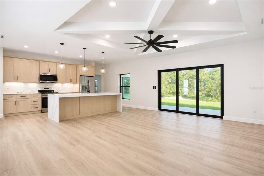 A modern kitchen with light wood cabinets, a waterfall island, and a large sliding glass door — 6231 ROWE STREET, ENGLEWOOD, FL
