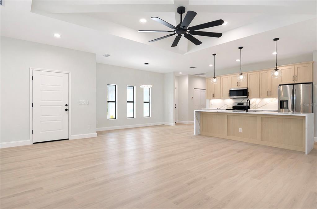 A bright, open-concept kitchen and living area features light wood flooring and a tray ceiling — 6231 ROWE STREET, ENGLEWOOD, FL