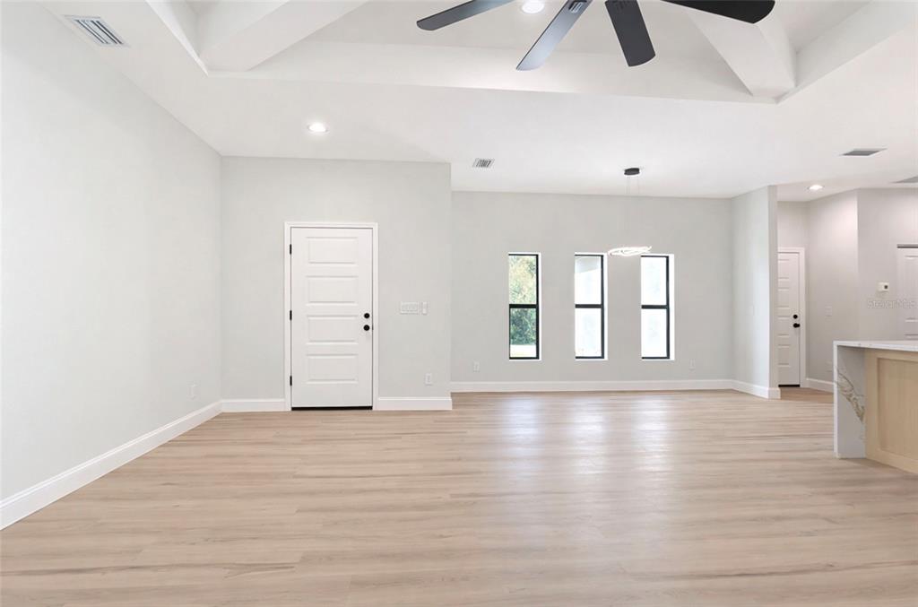 A bright, open-concept living area features light wood-look flooring, white walls, and a vaulted ceiling — 6231 ROWE STREET, ENGLEWOOD, FL