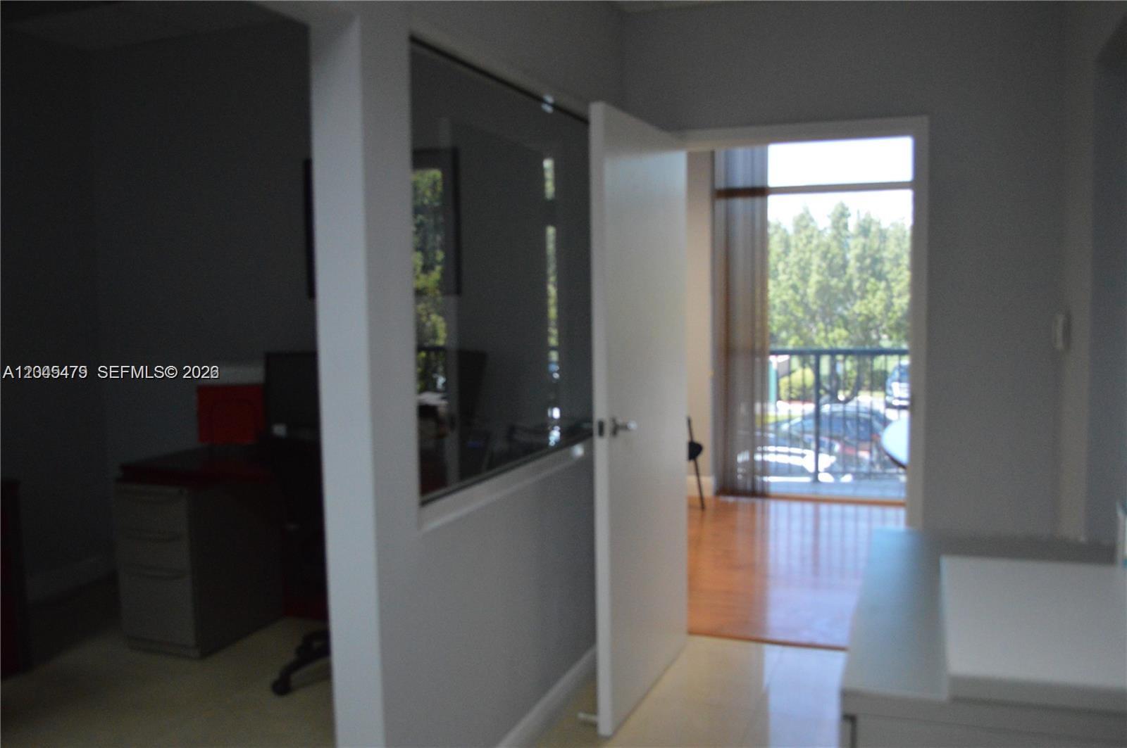 A view through an open doorway shows a room with a balcony and trees outside — MIAMI LAKES, FL