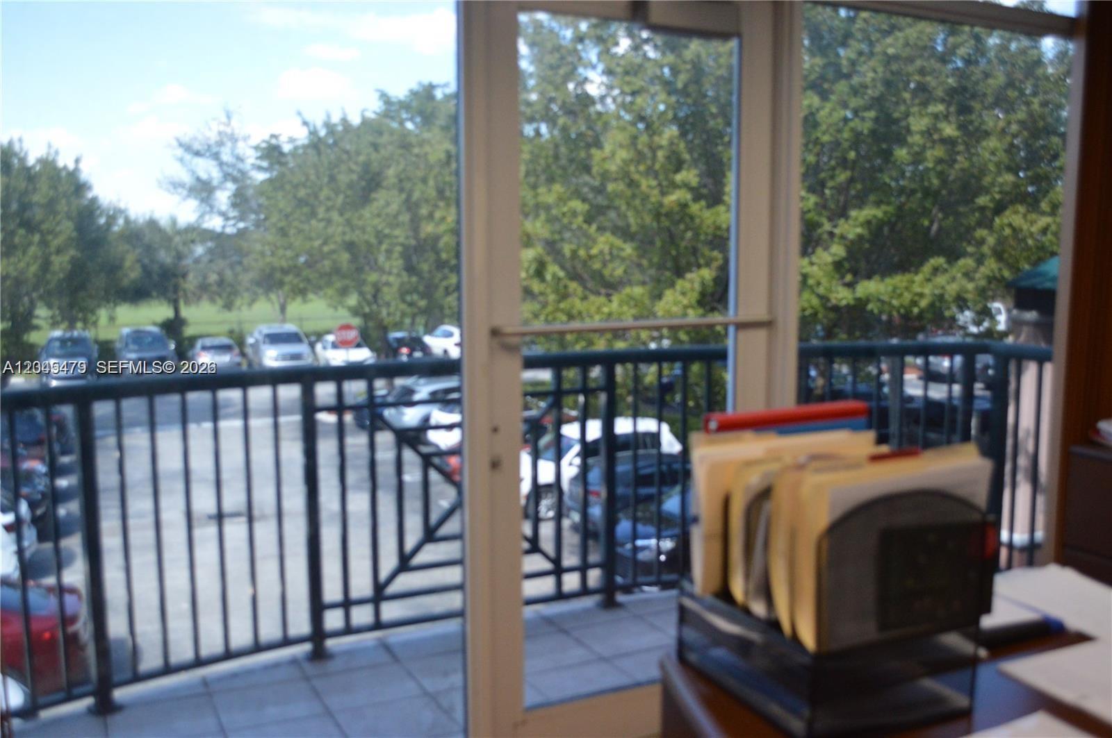 An office desk with a file organizer sits before a balcony door overlooking a parking lot — MIAMI LAKES, FL