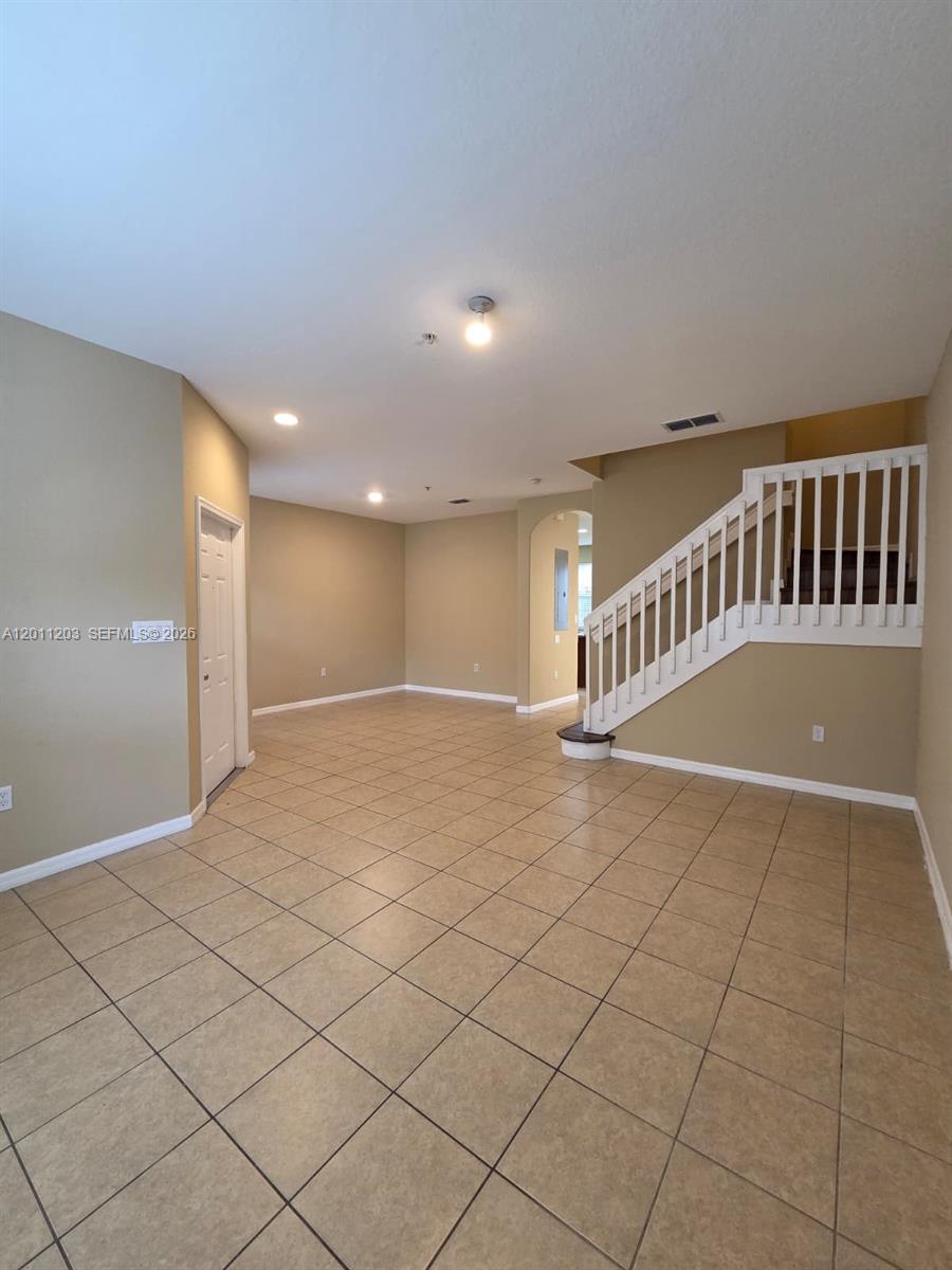 An empty room features beige walls, tiled flooring, and a white staircase with railings — 2851 W Prospect Rd # 404, Tamarac FL 33309, TAMARAC, FL
