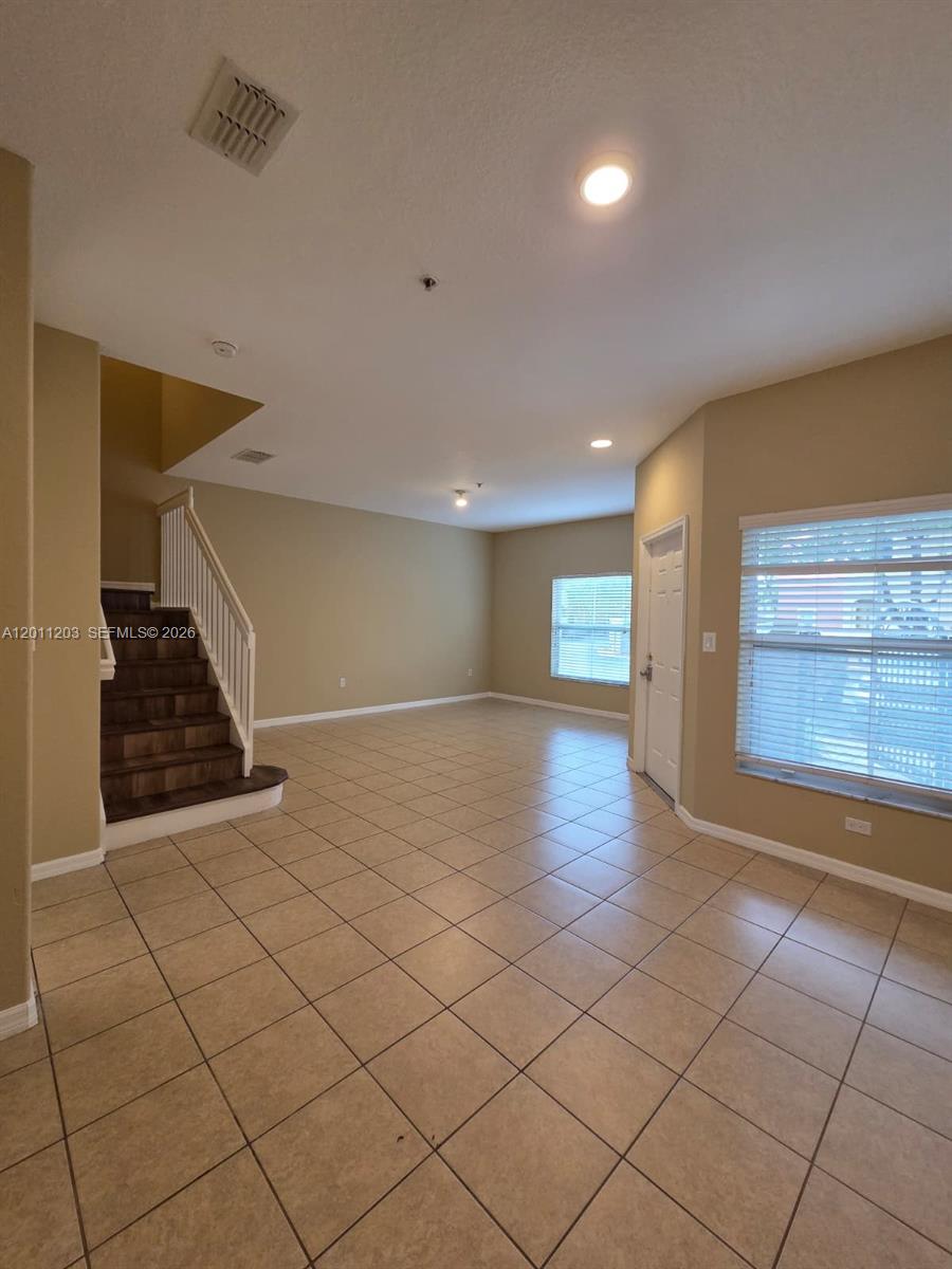 An open living area features beige walls, tile flooring, and a staircase with wooden steps — 2851 W Prospect Rd # 404, Tamarac FL 33309, TAMARAC, FL