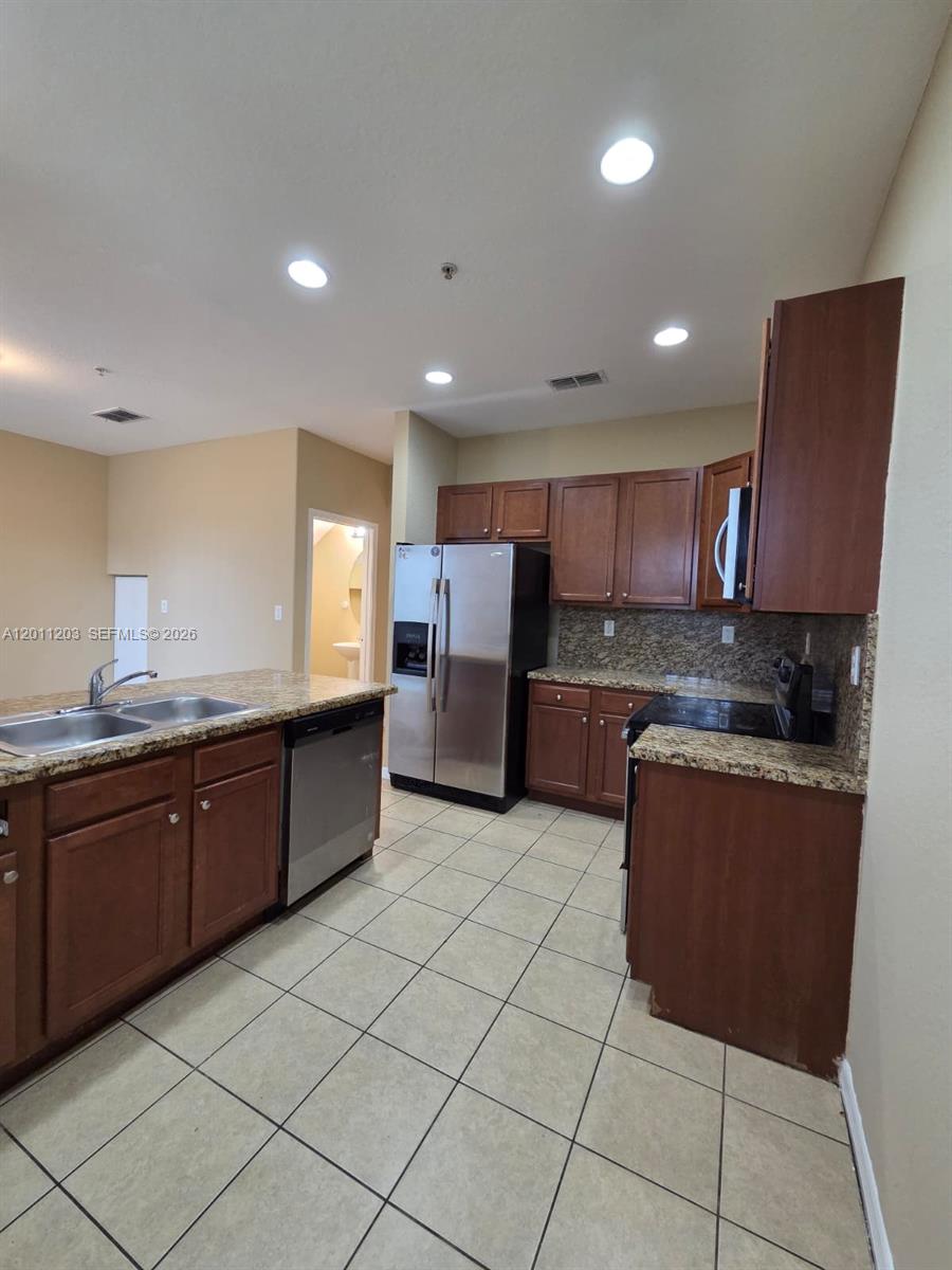 A kitchen features dark wood cabinets, granite countertops, stainless steel appliances, and tile flooring — 2851 W Prospect Rd # 404, Tamarac FL 33309, TAMARAC, FL